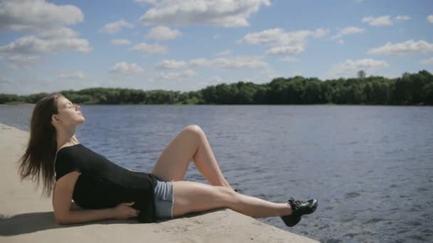 Young pretty woman sitting near river with closed eyes — Stock Video