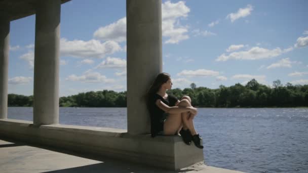 Jeune jolie femme assise près de la rivière regardant de côté — Video