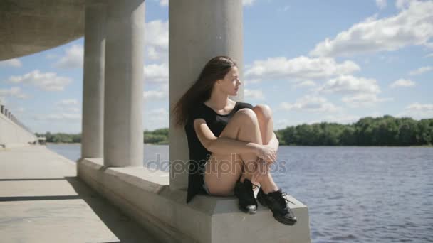 Молода красива жінка сидить біля річки, дивлячись вбік — стокове відео