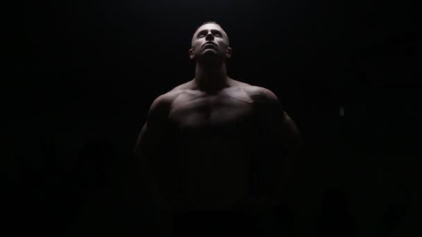 Bodybuilder poseren in donker — Stockvideo