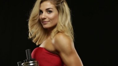 Genç sarışın bir kadın siyah üzerine poz dumbbells ile kırmızı mayo yerleştirmek ve kameraya benziyor. Dikey kaydırma