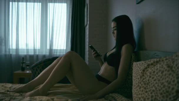 Młoda Kobieta Telefonem Komórkowym Siedząc Łóżku Zmierzchu Panoramowanie Poziome — Wideo stockowe