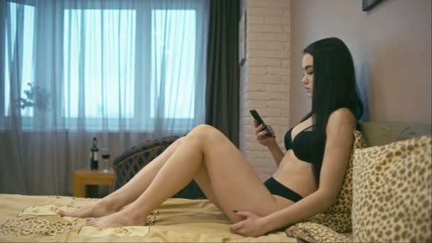 ベッドの上に座って携帯電話を持つ若い女性 水平方向のパン — ストック動画