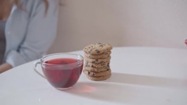 Masada ve kurabiyelerde kırmızı çay fincanı, arka planda kadın olan sığ alan derinliği