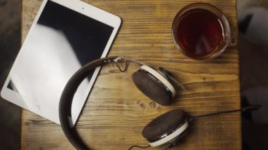 Tablet, kulaklık ve çay ahşap masada, ağır çekim.