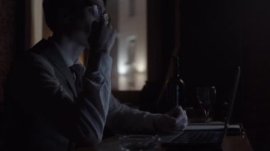 Genç adam laptopla çalışıyor ve sigara içiyor, ağır çekimde.