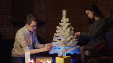 Genç adam ve kadın Noel ağacını süslüyorlar, ağır çekimde.