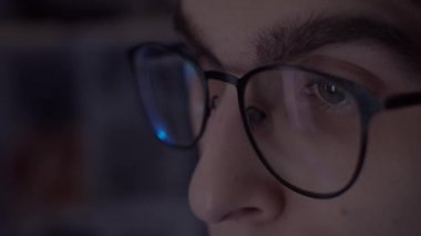 Bilgisayarda çalışan gözlüklü genç adam, gözlüklü monitörün yansıması, yavaş çekim, sığ alan derinliği