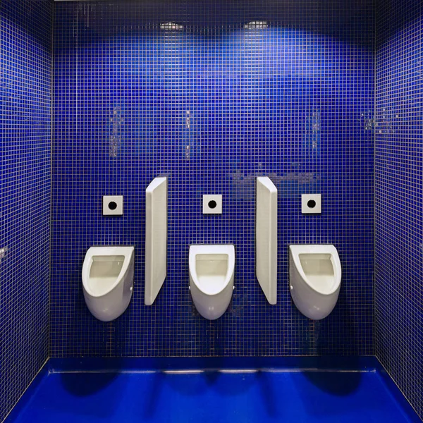Τρεις λευκοί ουρητηρίων σε δημόσια τουαλέτα άνδρες μπλε τοίχο. — Φωτογραφία Αρχείου