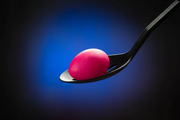 Pink Easter egg in a spoon in the center of the bright blue spot — Stock Photo, Image
