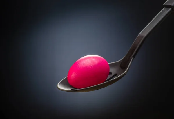 Pink Easter egg in a spoon in the center of the light spot on bl — Stock Photo, Image