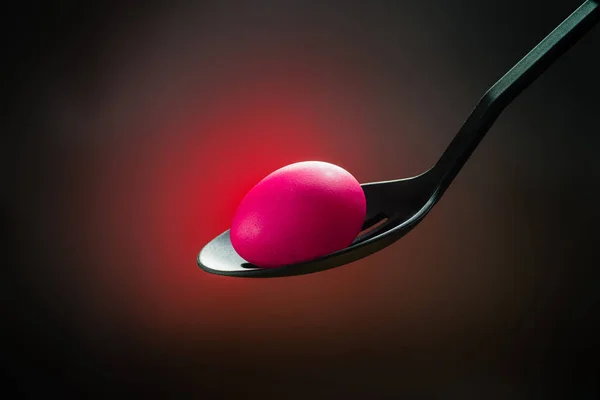 Pink Easter egg in a spoon in the centre a bright red spot on a — Stock Photo, Image