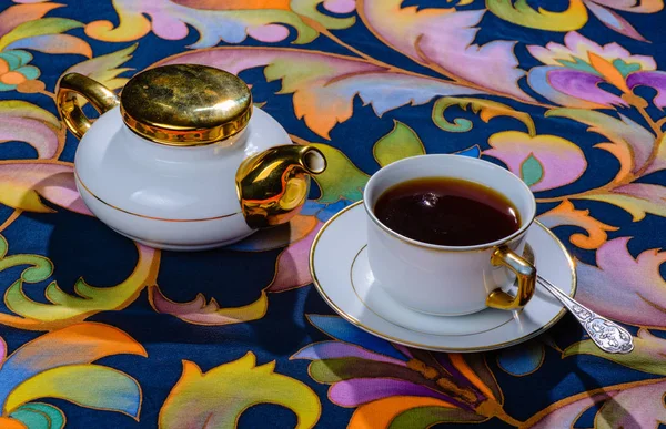 White tea Cup and teapot on the tablecloth with a bold pattern. — Stock Photo, Image