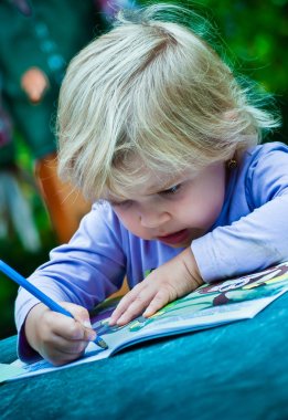 Küçük kız boyama albümde çizer.