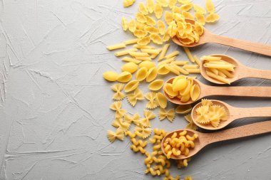 Farklı pişmemiş makarna ve gri masada tahta kaşıklar