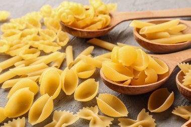 Farklı pişmemiş makarna ve gri masada tahta kaşıklar