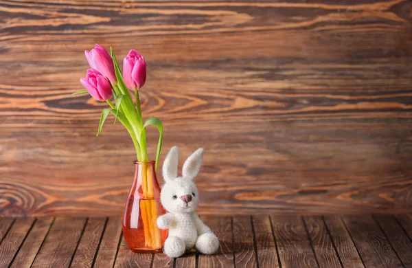 Vase with beautiful tulips and toy bunny on wooden table — Stock Photo, Image