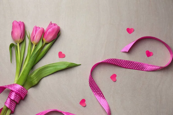 Ramo de hermosos tulipanes, cinta y corazones de papel sobre fondo claro — Foto de Stock