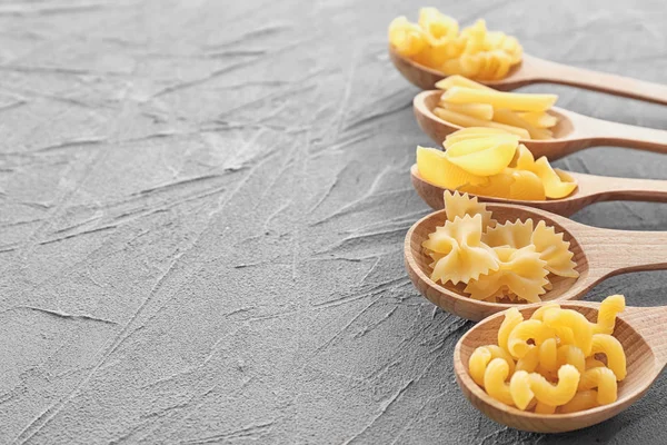 Wooden spoons with different uncooked pasta on grey table — Stock Photo, Image