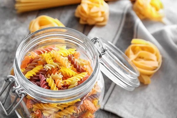 Jar with uncooked pasta on table