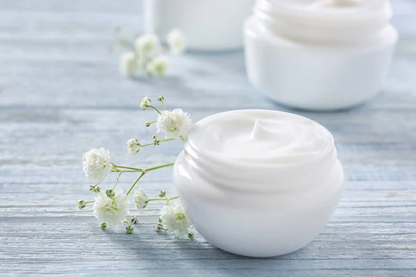 Vaso con crema e fiori su fondo di legno. Prodotti cosmetici per la cura della pelle — Foto Stock