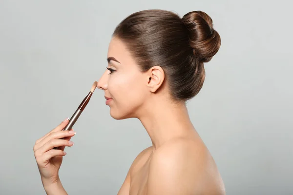 Vacker ung kvinna med borste för applicering av makeup på ljus bakgrund — Stockfoto