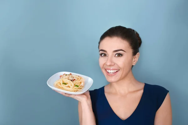 Jonge vrouw met een bord heerlijke pasta op kleur achtergrond — Stockfoto