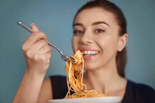 Young woman eating tasty pasta on color background — Stock Photo, Image