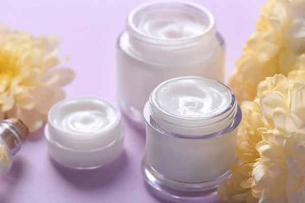 Jars with body cream and flowers on color background — Stock Photo, Image