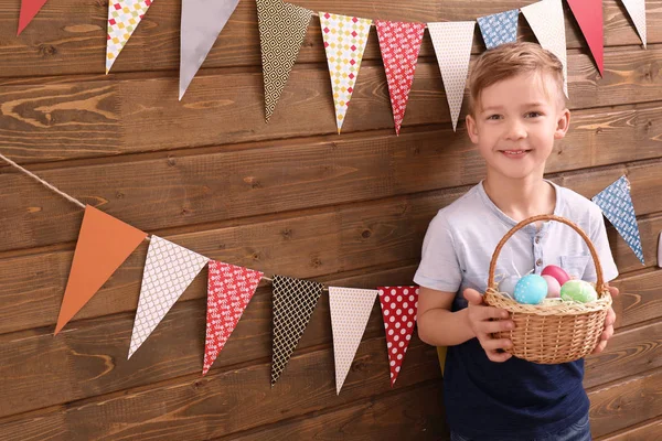 Aranyos kisfiú tartó kosár tele húsvéti tojás fa fal közelében díszített fél árbocok — Stock Fotó