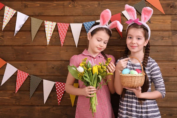 Niedlichen kleinen Mädchen mit Ostereiern und Blumen in der Nähe der Holzwand mit Party-Wimpeln dekoriert — Stockfoto