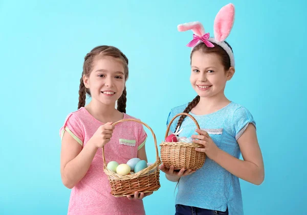 Niedliche kleine Mädchen halten Weidenkörbe mit Ostereiern auf farbigem Hintergrund — Stockfoto