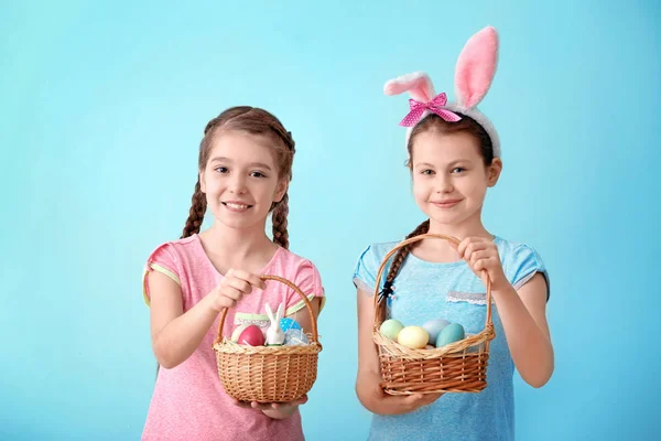 Meninas bonitos segurando cestas de vime com ovos de Páscoa no fundo de cor — Fotografia de Stock
