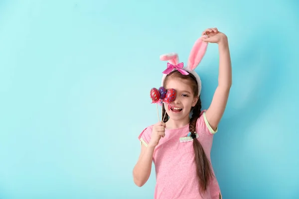 Cute little girl with bunny ears and Easter eggs on color background — Stock Photo, Image