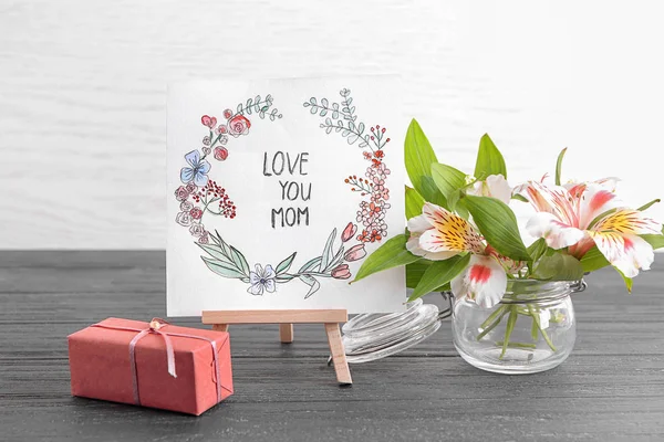 Card with phrase "Love you mom", flowers and gift box on table. Greeting for Mother's day — Stock Photo, Image