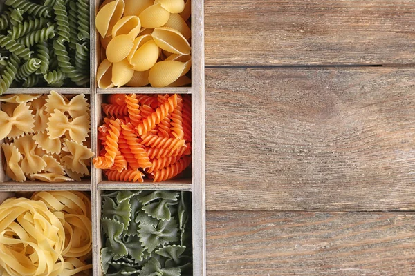 Wooden box with different raw pasta on table — Stock Photo, Image