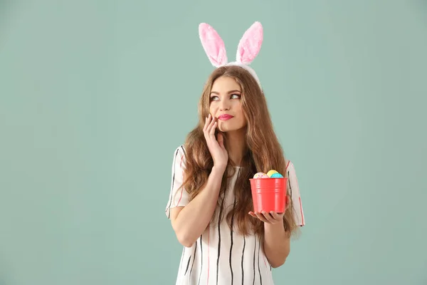 Krásná mladá žena s velikonoční vajíčka a uši zajíček na barvu pozadí — Stock fotografie