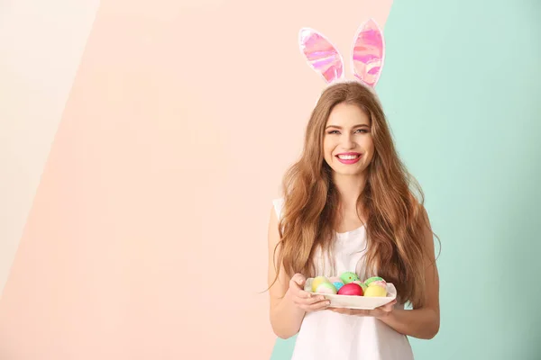 Beautiful young woman with Easter eggs and bunny ears on color background — Stock Photo, Image