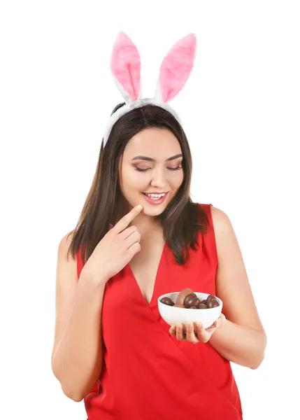 Bella giovane donna con uova di Pasqua al cioccolato e orecchie di coniglio su sfondo bianco — Foto Stock