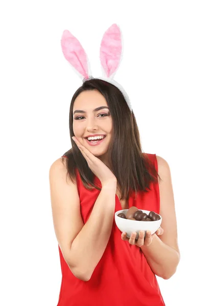 Bella giovane donna con uova di Pasqua al cioccolato e orecchie di coniglio su sfondo bianco — Foto Stock