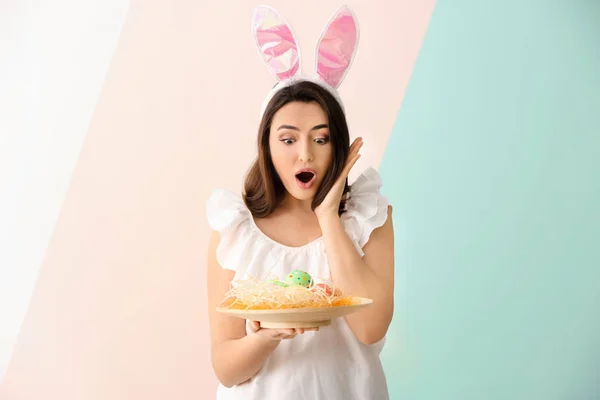 Jovem mulher emocional com ovos de Páscoa e orelhas de coelho no fundo de cor — Fotografia de Stock