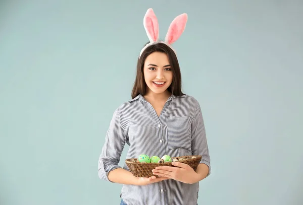 Krásná mladá žena s velikonoční vajíčka a uši zajíček na barvu pozadí — Stock fotografie