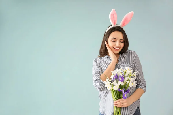 Vacker ung kvinna med Easter bunny öron och bukett blommor på färgbakgrund — Stockfoto