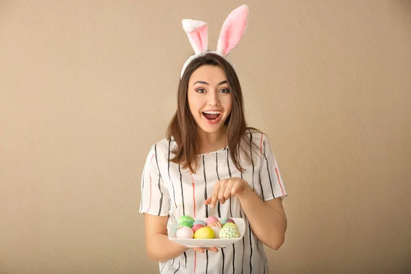 Beautiful young woman with Easter eggs and bunny ears on color background — Stock Photo, Image