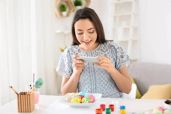 Young woman taking photo of painted Easter eggs at home — Stock Photo, Image