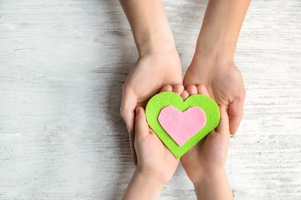 Mani di madre e bambino con cuore in feltro su sfondo di legno — Foto Stock