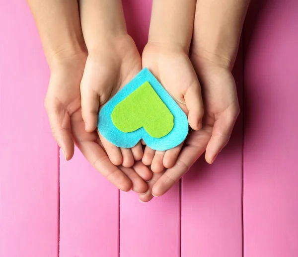 Hands of mother and child with felt heart on color background — Stock Photo, Image