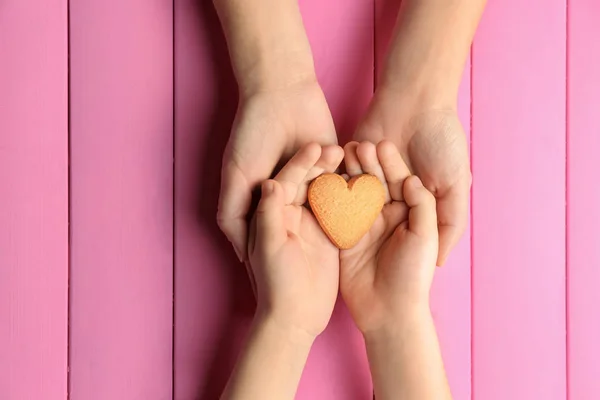 Mani di madre e bambino con biscotti a forma di cuore su sfondo a colori — Foto Stock