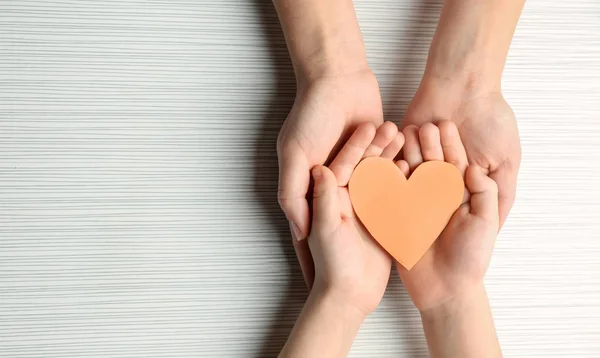 Hands of mother and child with paper heart on light background — Stock Photo, Image