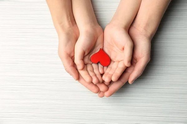 Hands of mother and child with small red heart on light background — Stock Photo, Image
